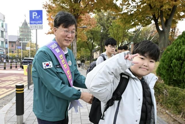 이민근 안산시장(사진 왼쪽)이 학현초등학교 앞에서 ‘스쿨존 어린이 교통안전 캠페인’을 진행하며 등교하는 어린이의 가방에 '홍이 키링'을 달아주고 있다.